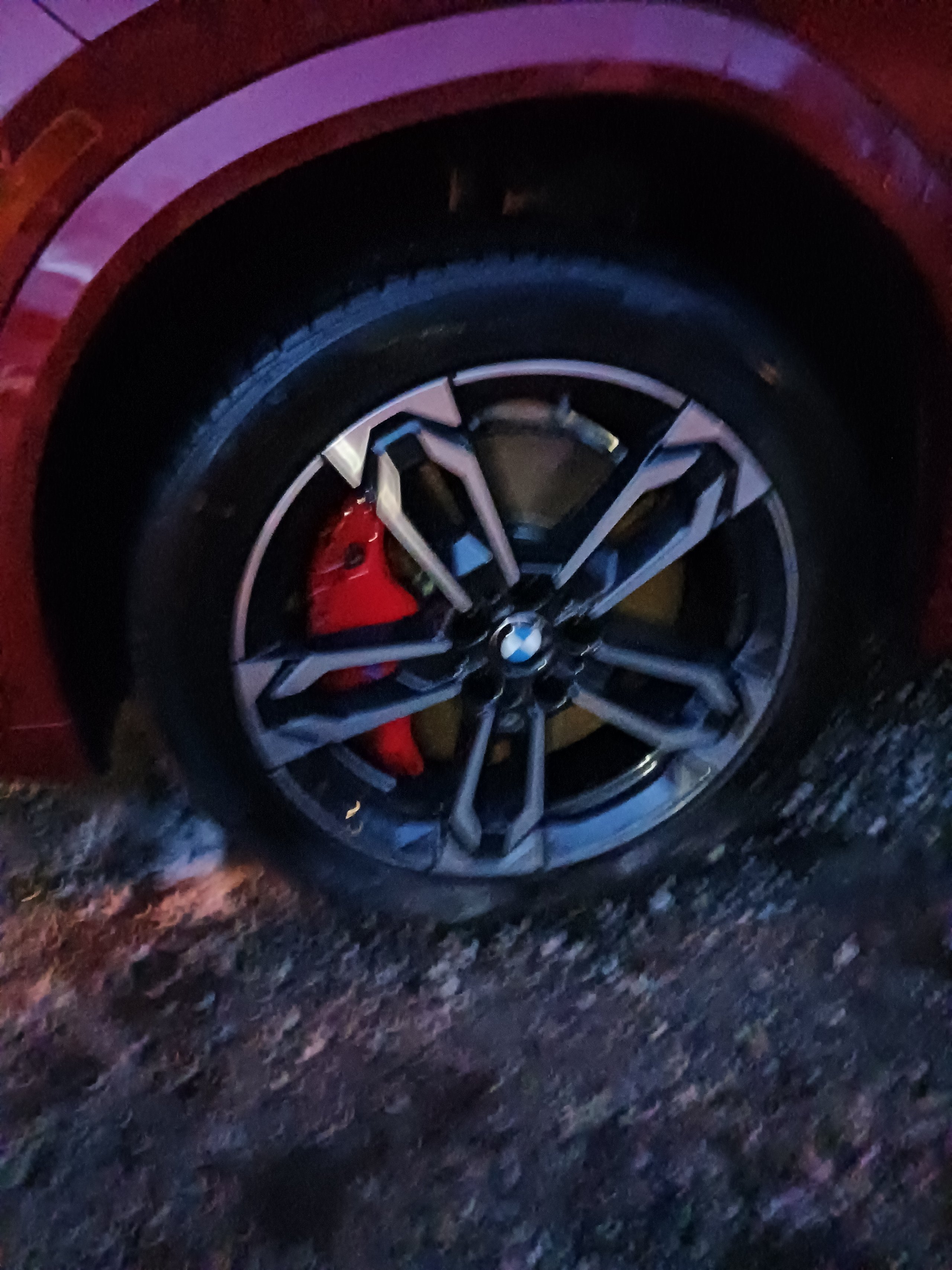 Close-up of a car wheel with dark alloy rim and red brake caliper visible through the spokes