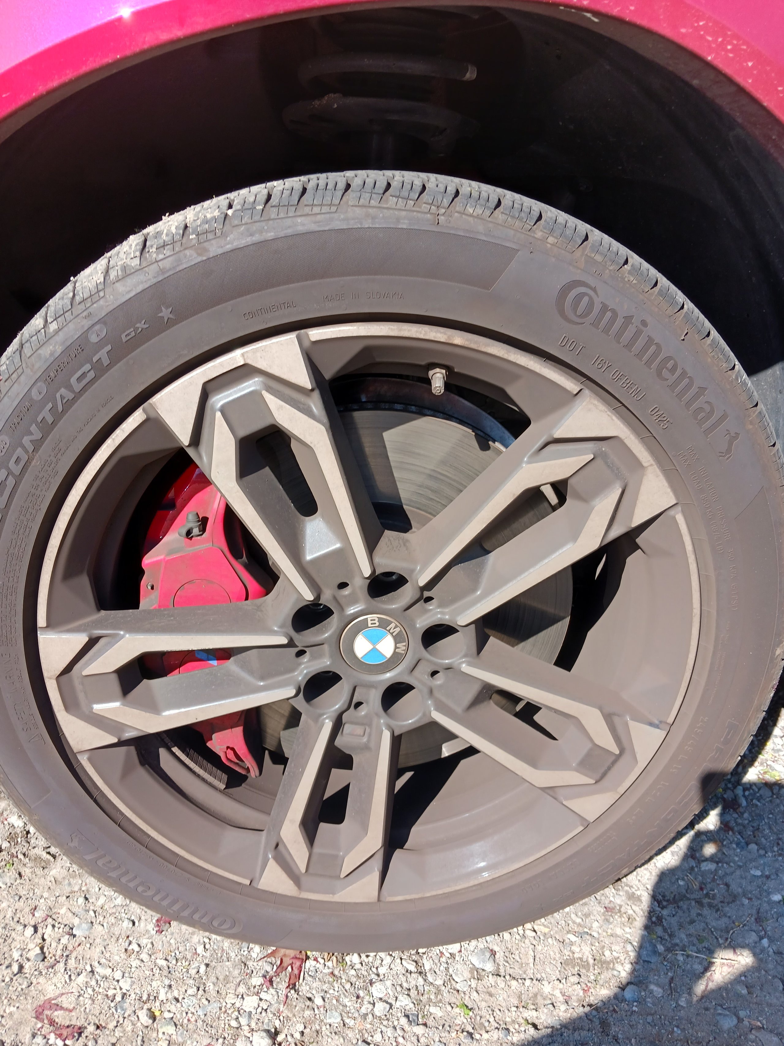 Close-up of a car wheel with silver alloy rim, Continental tire, and bright pink brake caliper visible behind the spokes
