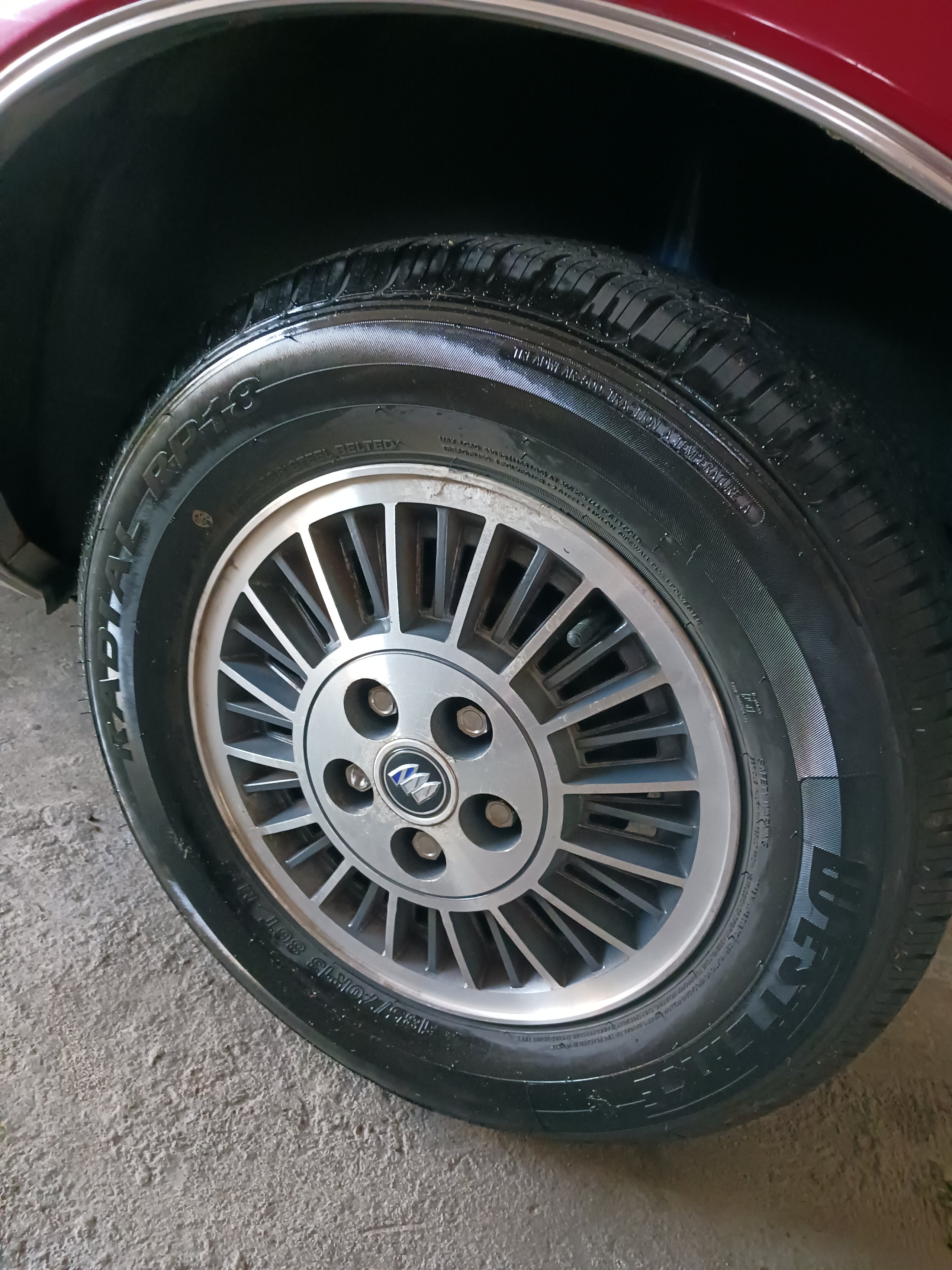 Close-up of a car wheel with silver and black alloy rim and black tire mounted on a maroon-colored vehicle