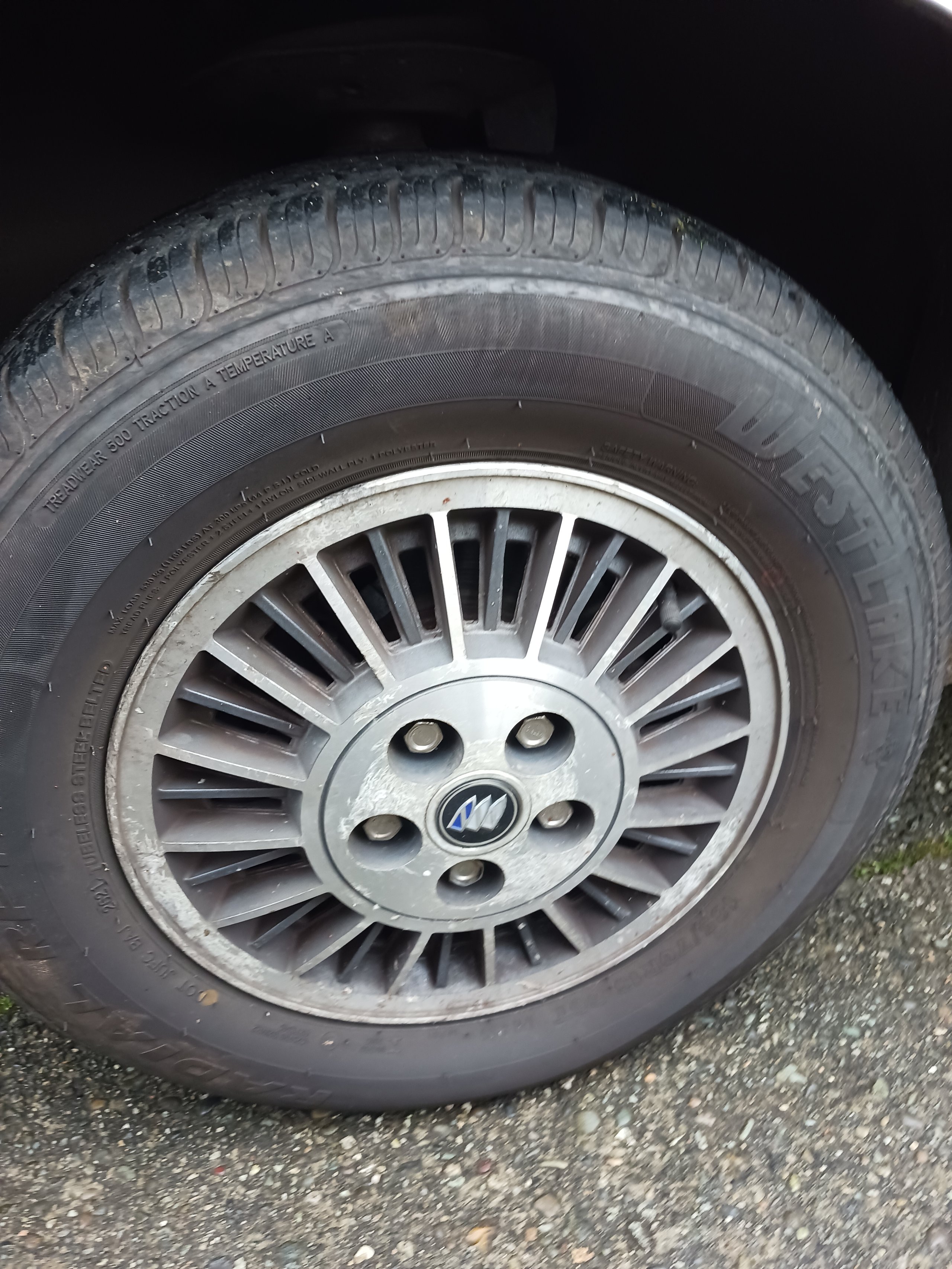 Close-up of a car wheel with silver alloy rim and radial tread tire on pavement